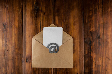 An email sign with white blank paper on a craft envelope lies on a vintage wooden table. Concept e-mail message letter. Top view with copy space