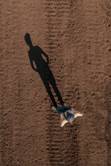 Female farmer standing in ploughed field casting long shadow on the ground