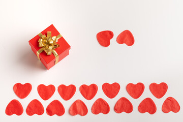 Two rows of paper red hearts. A box with a gift bow and two hearts next to a white background,