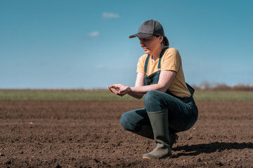 Naklejka na ściany i meble Female farmer agronomist checking the quality of ploughed field soil before sowing season