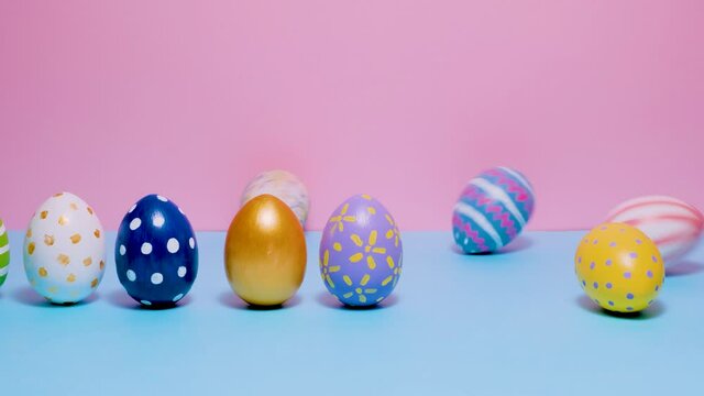 Video of Happy Easter. Colorful painted Easter eggs roll and knock each other on a blue and pink background. Hello spring and easter concept. 4k video.
