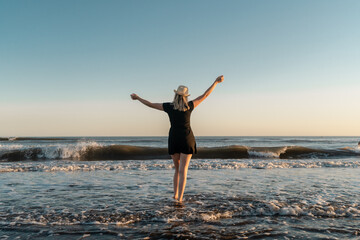Obraz premium Happy woman enjoying her freedom with open arms on the seashore at sunset.