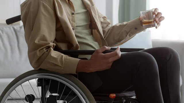 Unrecognizable Disabled Black Man In Wheelchair Drinking Whiskey At Home