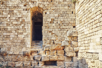 Fototapeta na wymiar Weathered ancient Rhodes fortress brick and stone wall with empty arch doorway under bright sunlight in summer Greece