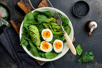 Fresh vegetable salad with avocado, asparagus, crumpled eggs with black sesame seeds and spinach on plate on light slate, stone or concrete background. Balanced lunch in bowl. Top view. Mock up.