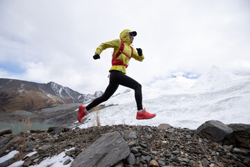 Woman trail runner cross country running up hill to winter snow mountain top