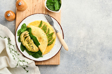 Omelette or omelet stuffed with asparagus, avocado and spinach leaves for breakfast on white plate over white slate, stone or concrete background. Balanced and tasty morning food. Mock up. Top view.