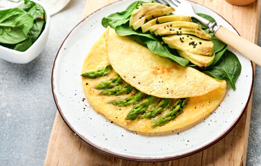 Omelette or omelet stuffed with asparagus, avocado and spinach leaves for breakfast on white plate over white slate, stone or concrete background. Balanced and tasty morning food. Mock up. Top view.