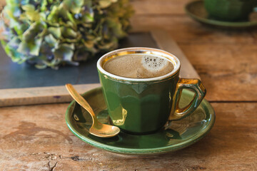 Green vintage cup of coffee on old wooden table, hydrangea flowers close up.