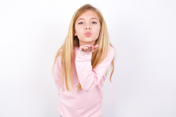beautiful caucasian little girl wearing pink hoodie over white background looking at the camera blowing a kiss with hand on air being lovely and sexy. Love expression.