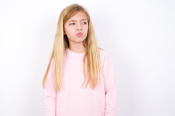beautiful caucasian little girl wearing pink hoodie over white background, looks pensively aside, plans actions after university, imagines what to do Thinks over about new project.
