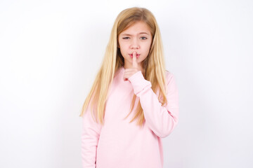 beautiful caucasian little girl wearing pink hoodie over white background makes hush gesture, asks be quiet. Don't tell my secret or not speak too loud, please!