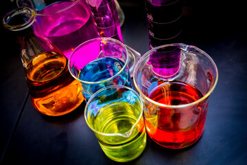 Various laboratory beakers and cylinders filled with colorful liquids isolated on a black table and background