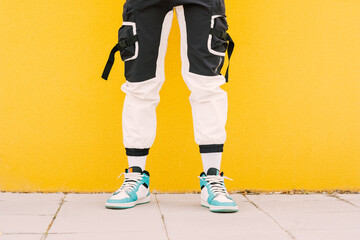 Naklejka premium Unrecognizable young trendy and fashionable man against a yellow wall wearing a black and white pants with basket sneakers
