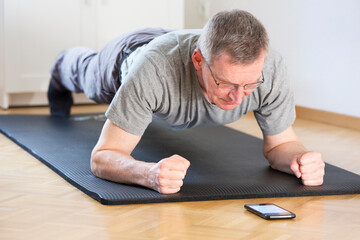 Fototapeta na wymiar Mature man doing fitness exercise at home while looking at a smartphone