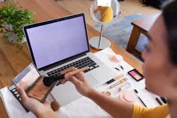 Mixed race gender fluid man using makeup making vlog with laptop, copy space screen