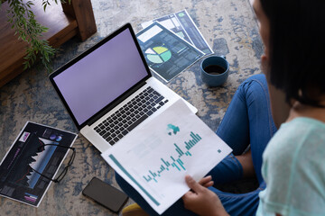 Mixed race gender fluid man working at home sitting on floor using laptop, copy space screen