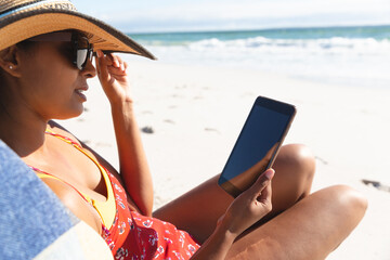 Mixed race woman on beach holiday sitting in deckchair using tablet
