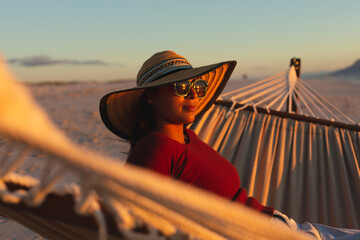 Mixed race woman on beach holiday sitting in hammock during sunset