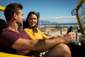 Happy caucasian couple sitting in beach buggy by the sea talking