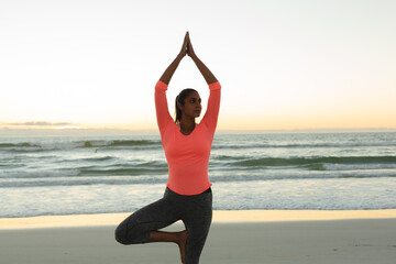 Fototapeta na wymiar Mixed race woman on beach practicing yoga at sunset