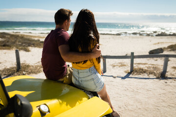 Happy caucasian couple sitting in beach buggy looking towards sea