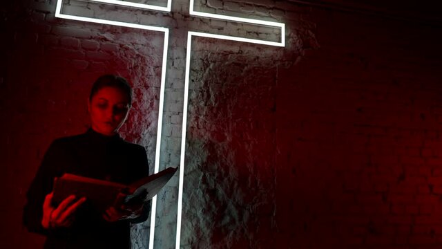 A young monk reads the Bible against a neon cross in red. halloween party