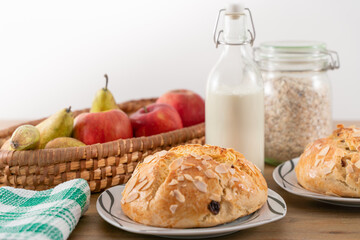Freshly baked, homemade sweet cake with almonds and raisins on wooden table. Easter loaf. Basket with pears and apples. Vintage bottle of milk. Green cloth.