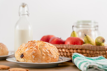 Freshly baked, homemade sweet cake with almonds and raisins on wooden table. Easter loaf. Basket with pears and apples. Vintage bottle of milk. Green cloth and ginger cookies.