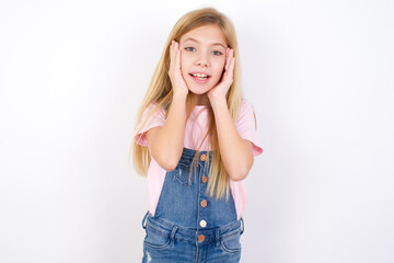 Fototapeta premium beautiful Caucasian little girl wearing denim overalls over white background Pleasant looking cheerful, Happy reaction