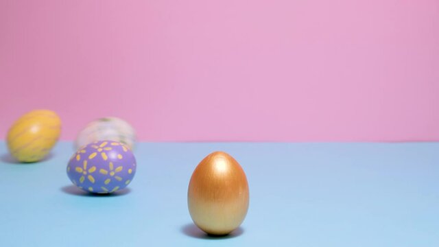 Video of Happy Easter. Colorful painted Easter eggs roll and knock each other on a blue and pink background. Hello spring and easter concept. 4k video.