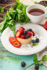 Sweet tart with fresh raspberry strawberry blackberry and cup of tea on the table