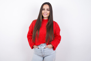 Portrait of successful young beautiful brunette woman wearing red knitted sweater over white wall, smiling broadly with self-assured expression. Confidence and business concept.