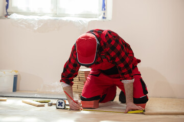 Man laying parquet flooring, worker joining parquet floor. The builder, man is engaged in laying laminate wood floor in the room - repair and finishing work