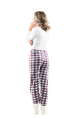 Back view of young woman in pajamas relaxing at home talking on the cell phone. Full body length isolated on white background.