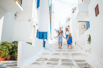 Family vacation in Europe. Parents and kids at street of typical greek traditional village with white walls and colorful doors on Mykonos Island