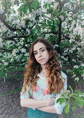 Close-up portrait of a girl with long hair among the branches of a blossoming apple tree