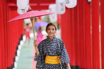 woman in kimono holding umbrella walking into at the shrine red gate, in Japanese garden.