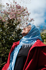 Muslim mature woman wearing hijab looking relaxed to the sun in a beautiful spring day in a London Park.
