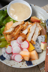 Close up fried chicken salad, cream and vegetable salad dressing, reddish cantaloupe on a light brown background.