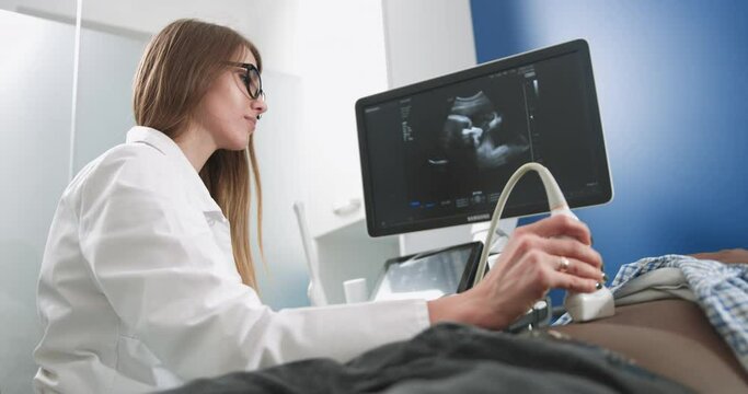 Focused female doctor performs ultrasound examination of internal organs of her black male patient for diagnostic of stomach desease at the modern medical office
