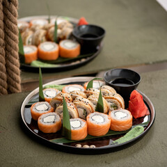 Set of sushi rolls Philadelphia with salmon and eel on black platter with wasabi and ginger. Asian or Japanese food, Oriental cuisine. Soft focus.