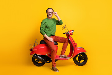 Fototapeta na wymiar Photo of bearded man ride scooter look camera wear glasses green sweater pants shoes isolated yellow color background