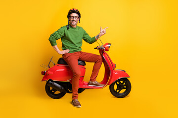 Fototapeta na wymiar Photo of guy drive scooter direct finger empty space wear helmet glasses green sweater pants isolated yellow color background