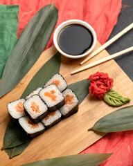 Beautiful sushi roll serving. Rice, salmon and nori seaweed platter on cutting board with soy sauce, wasabi, ginger and chopsticks on it. Traditional oriental cuisine. High angle view.