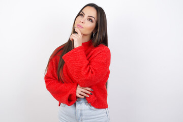 Shocked young beautiful brunette woman wearing red knitted sweater over white wall shows something little with hands, demonstrates size, opens mouth from surprise. Measurement concept.