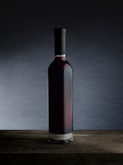 Fototapeta na wymiar A bottle of red wine, on a wooden empty tabletop against a dark wall background. Wine bottle mockup.