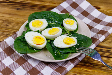 Boiled eggs with fresh spinach leaves and sesame seeds on wooden table