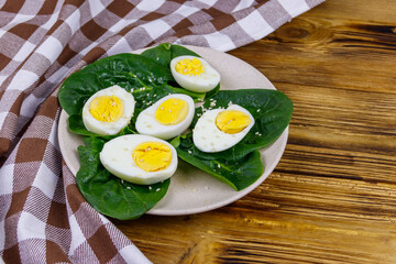 Boiled eggs with fresh spinach leaves and sesame seeds on wooden table