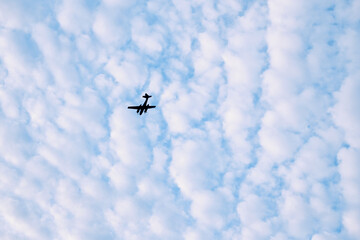 Airplane in blue sky with clouds in background.